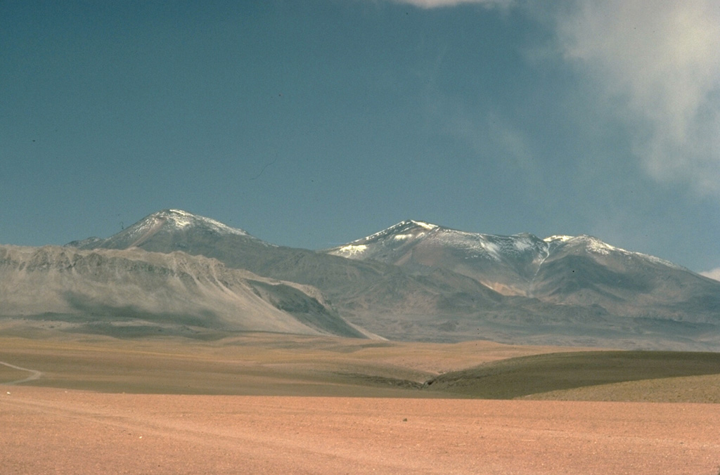 Cerros de Tocorpuri, seen here from the west, is a Pleistocene stratovolcano complex on the Chile-Bolivia border.  A Holocene lava dome on its western foot, Cerro la Torta, forms the light-colored ridge at the left foreground.  The circular, roughly 5 cu km Cerro la Torta was erupted from a central vent and is surrounded by a flat-topped surface with wrinkled flow ridges.  The flow terminates in steep, talus-covered margins about 150-m high.  Lava extrusion was preceded by minor silicic explosive eruptions. Copyrighted photo by Katia and Maurice Krafft, 1983.