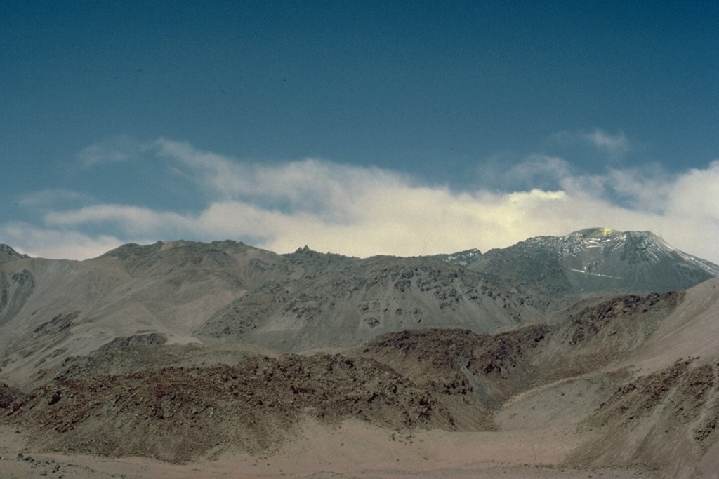 The complicated structure of Volcán Putana can be seen in this view from the NW.  The volcanic complex was formed almost entirely by lava effusion.  Thick viscous lava flows have issued from both summit and flank vents.  Early lava flows mantling an older Pleistocene edifice were longer, whereas the younger flows are short and stubby, rarely exceeding 3 km in length.  A road leads to a sulfur mine near the summit (extreme right). Copyrighted photo by Katia and Maurice Krafft, 1983.