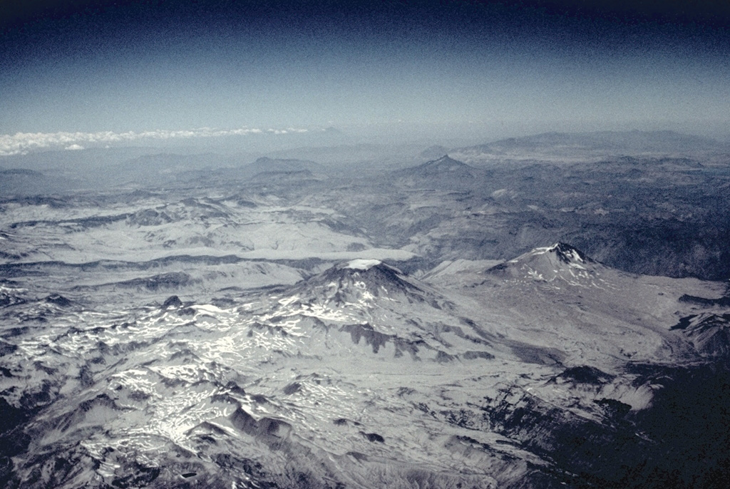 Descabezado Grande (center) and Cerro Azul (middle right), seen here from the NW, are the most prominent features of a large volcanic field.  The most active of the two large stratovolcanoes is 3810-m-high Cerro Azul.  Quizapú, a vent that formed in 1846 on the northern flank of Cerro Azul, was the source of one of the world's largest explosive eruptions of the 20th century in April 1932.  The eruption created a 600-700 m wide crater and ejected 9.5 cu km of dacitic tephra.  The only historical eruption of Descabezado Grande took place later in 1932. Photo by Jeff Post, 1988 (Smithsonian Institution).
