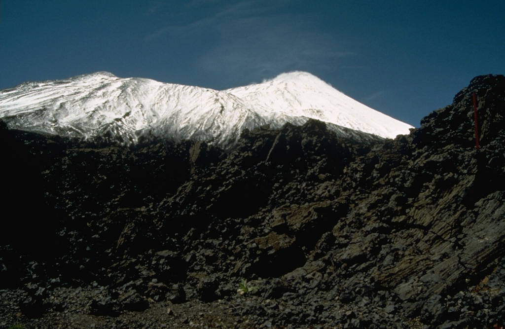 Antuco volcano, seen here from the NW, has a complicated history beginning with construction of an andesitic stratovolcano during the Pleistocene.  Edifice failure at the beginning of the Holocene produced a large debris avalanche that traveled down the Río Laja to the west.  The collapse left a large horseshoe-shaped caldera whose NW rim forms the ridge descending to the right.  The steep-sided modern basaltic cone (upper right) has grown 1000 m since then.  Moderate explosive eruptions were recorded in the 18th and 19th centuries. Photo by Norm Banks, 1990 (U.S. Geological Survey).
