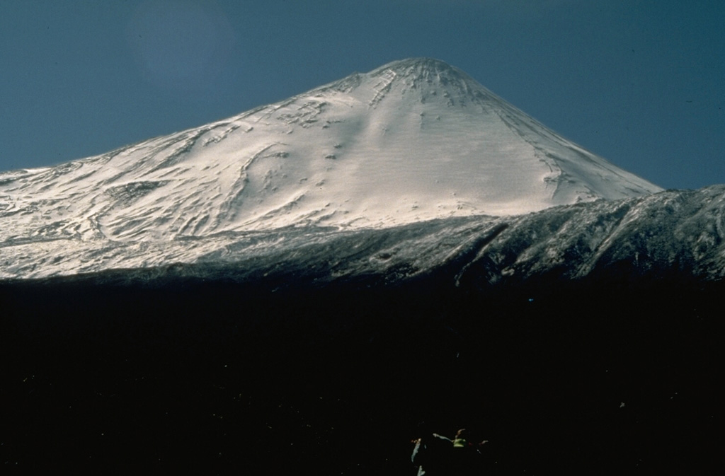 The snow-capped modern summit of 2979-m-high Antuco volcano rises above the rim of a large horseshoe-shaped caldera, whose WNW rim forms the flat ridge just above the snow line.  The caldera was formed by collapse of an older Antuco volcano at the beginning of the Holocene.  The 1-km-high modern cone subsequently grew at the head of the scarp.  Eruptions from both summit and flank vents have occurred during the 19th and 20th centuries. Photo by Norm Banks, 1990 (U.S. Geological Survey).