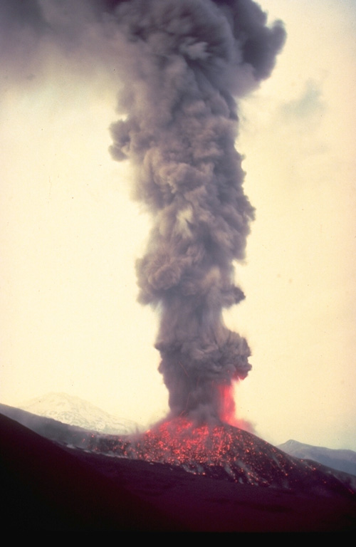 An ash-rich eruption column, incandescent at its base, rises above Navidad cinder cone on the NE flank of Lonquimay volcano in January 1989.  Still-glowing volcanic bombs litter the flanks of the cone.  Tolguaca volcano appears at the left in this view from the SE.  Soon after the start of the eruption on December 25, 1988, lava effusion began, producing a lava flow that by the time the eruption ended in January 1990 had traveled 10 km down the NE flank. Copyrighted photo by Katia and Maurice Krafft, 1989.