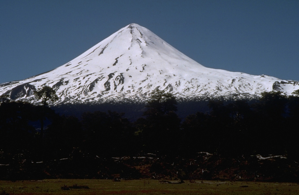 Llaima, one of Chile's largest and most active volcanoes, has a symmetrical profile when seen from the north.  The massive, 3125-m-high, glacier-covered stratovolcano is constructed primarily of accumulated lava flows and has a volume of 400 cu km.  Volcán Llaima contains two historically active craters, one at the summit and the other to the SE.  More than 40 scoria cones dot the volcano's flanks.  Frequent moderate explosive eruptions, a few of which were accompanied by lava flows, have been recorded since the 17th century.  Photo by Norm Banks, 1990 (U.S. Geological Survey).