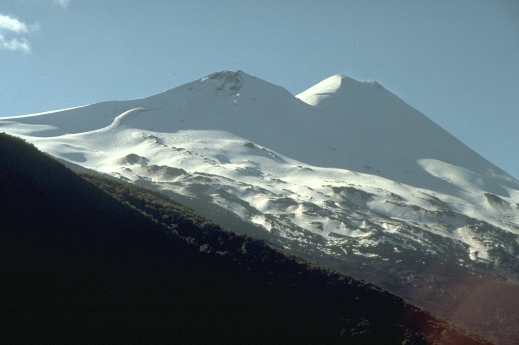 Seen from the SE, Llaima volcano has a twin-peaked profile.  Historical eruptions have occurred from craters topping both the 3125-m-high summit cone of Llaima (right) and the 2920-m-high SE cone (left).  About 50 eruptions have occurred from Volcan Llaima, one of Chile's most active volcanoes, since its first historical eruption in 1640.  Frequent moderate explosive eruptions are often accompanied by lava flows.  Mudflows sweeping down the flanks of the glaciated volcano have damaged villages at its foot. Photo by Norm Banks, 1990 (U.S. Geological Survey).