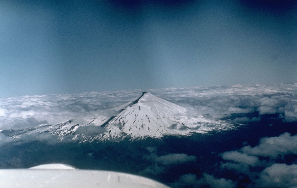 Snow-capped Villarrica, one of Chile's most active volcanoes, is seen here in 1984 with a dark-colored lava flow descending its flank.  Plinian eruptions and pyroclastic flows have been produced during the Holocene from this dominantly basaltic volcano, but historical eruptions have consisted largely of mild-to-moderate explosive activity with occasional lava effusion.  Lahars from the glacier-covered volcano have damaged towns on its flanks.    Photo by Hugo Moreno, 1984 (University of Chile).