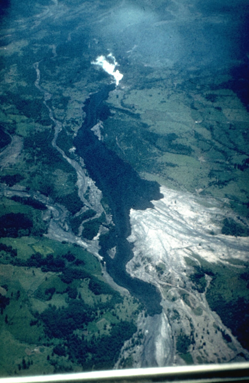 A dark lava flow descends the Chaillupén river on the SW flank of Villarrica volcano towards Lake Calafquén during an eruption in 1971.  The lava flow overrides light-colored mudflow deposits produced earlier during the eruption, which began on October 29.  On November 29 lava effusion and pyroclastic cone formation began.  Three basaltic lava flows were emitted on the SW flank during December 3-20.  The eruption culminated on December 29, when lava flows melted ice, producing lahars that swept the volcano's flanks and caused 15 fatalites.  The eruption lasted until January 10.  Photo by Hugo Moreno, 1971 (University of Chile).