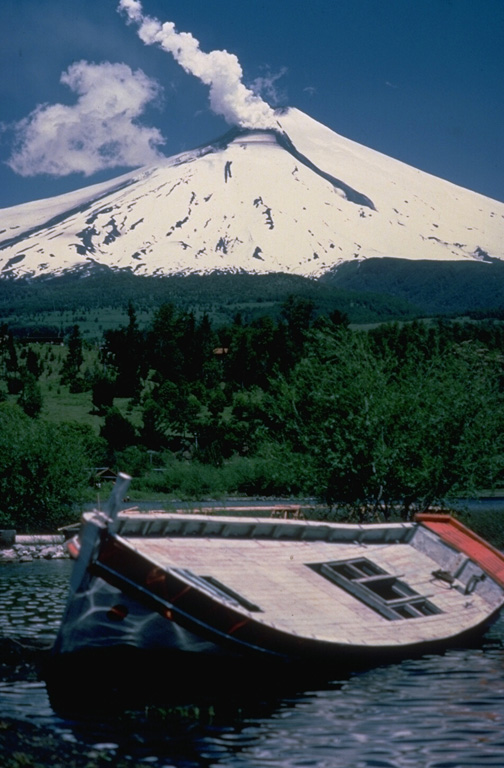 Villarrica, one of Chile's most active volcanoes during historical time, rises above Lake Villarrica.  This December 1984 view from the NE shows steam rising from the summit crater and a lava flow descending the glacier-covered flanks of the volcano.  This dominantly basaltic volcano has produced plinian eruptions and pyroclastic flows during the Holocene, but historical eruptions have consisted largely of mild-to-moderate explosive activity with occasional lava effusion.  Lahars from the glacier-covered volcano have damaged towns on its flanks. Copyrighted photo by André Demaison, 1984 (courtesy of Katia and Maurice Krafft).