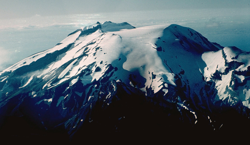 Calbuco is one of the most active volcanoes of the southern Chilean Andes.  The isolated volcano rises to 2003 m south of Lake Llanquihue, which is visible at the upper right.  The summit ridge (center) of the volcano is the remnant of an older volcano that collapsed during the late Pleistocene and produced a 3 cu km debris avalanche that reached the lake.  Subsequent eruptions generated andesitic lava flows, breccias, and tuffs that filled the scarp and were subsequently topped by an historical lava-dome complex (right center). Photo by Hugo Moreno (University of Chile).