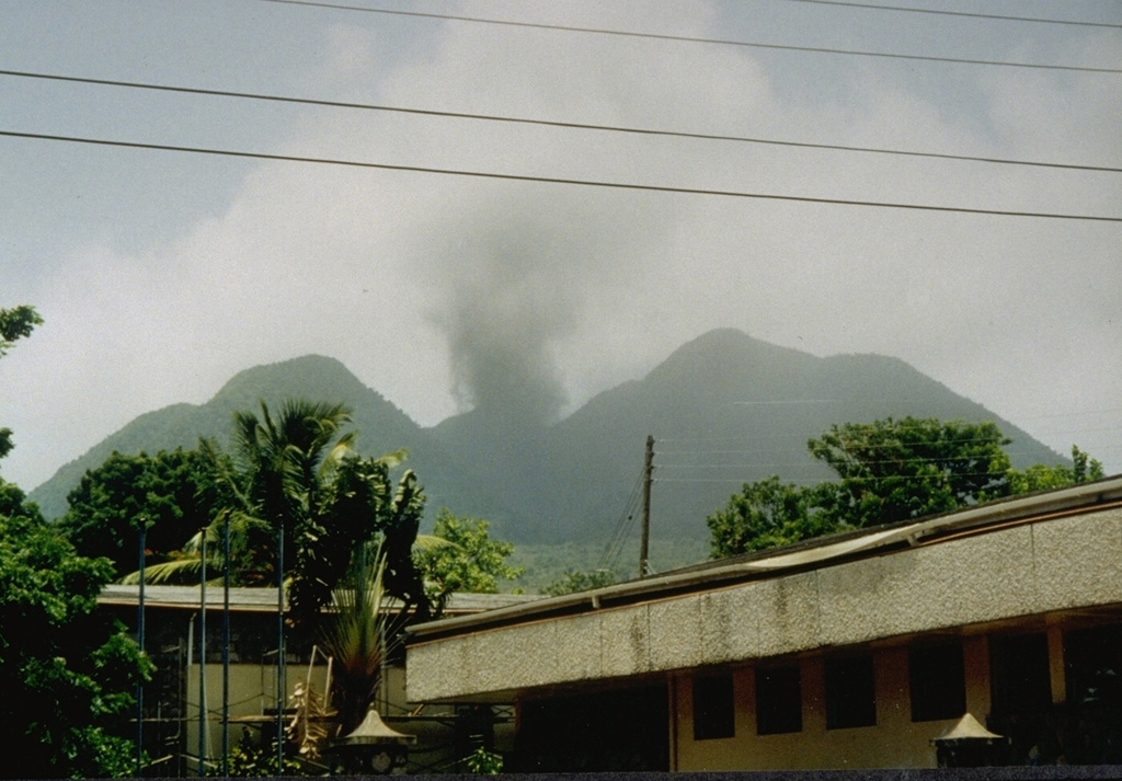 An ash plume rises above the summit of Soufrière Hills volcano on July 19, 1995, the day after the start of a major eruption that began in 1995.  This view was taken from the center of Plymouth, the capital city of Montserrat, which is located along the west coast only 4 km from the summit.  The eruption column is originating from a vent on the flank of a lava dome inside English's Crater. Photo by Micole and Adam Dennis, 1995.
