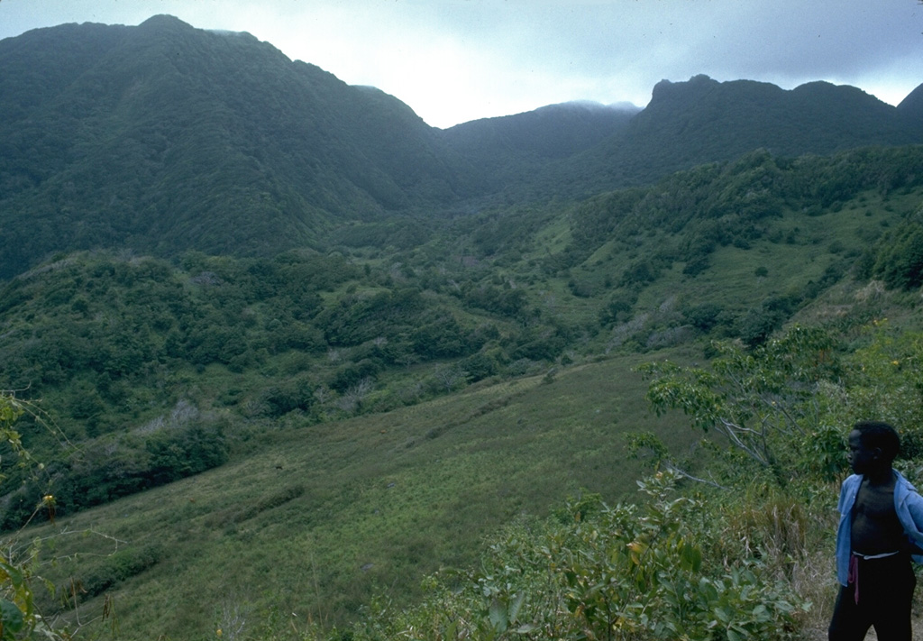 Castle Peak lava dome, on the right skyline, was formed about 350 years ago during the last eruption of Soufrière Hills volcano prior to the 20th century.  Seen here in 1977 from the Tar River valley on the east side of the volcano, the Castle Peak dome was constructed within a 1-km-wide horseshoe-shaped crater, whose southern wall forms the left skyline.  The high point at the left is Perche's Mountain lava dome. Photo by Richard Fiske, 1977 (Smithsonian Institution).