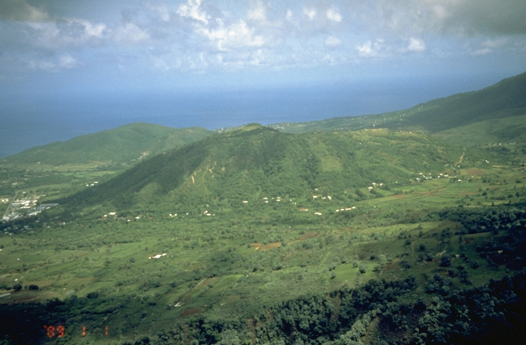 St. George's Hill (center) and Garibaldi Hill (along the coast to the left) are two Pleistocene lava domes on the NW flank of Soufrière Hills volcano.  Pyroclastic flows from a lava dome growing in the summit crater flowed down the NW flank beginning in August 1997 and banked up against St. George's Hill before turning to the left and sweeping into the sea through the center of Plymouth, the capital city of the island of Montserrat.  This aerial photo was taken in August 1995 from above the west flank of the volcano. Photo by Cynthia Gardner, 1995 (U.S. Geological Survey).