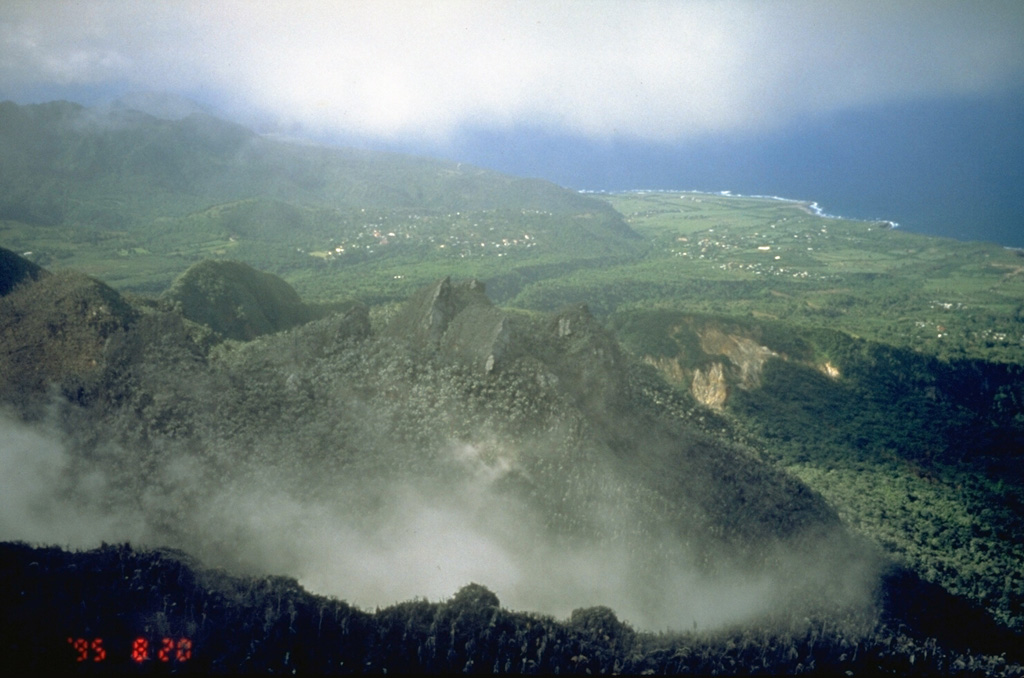 Castle Peak lava dome (center) was formed about 350 years ago during the last eruption of Soufrière Hills prior to 1995.  The walls of horseshoe-shaped English's Crater are seen in front of and behind the dome.  This August 20, 1995, photo from the SW shows a light covering of ash on Castle Peak from early stages of the eruption that began in 1995.  The village of Harris, along the Paradise River in the center distance, was destroyed by pyroclastic flows in June 1997 that reached to within 500 m of the sea. Photo by Cynthia Gardner, 1995 (U.S. Geological Survey).