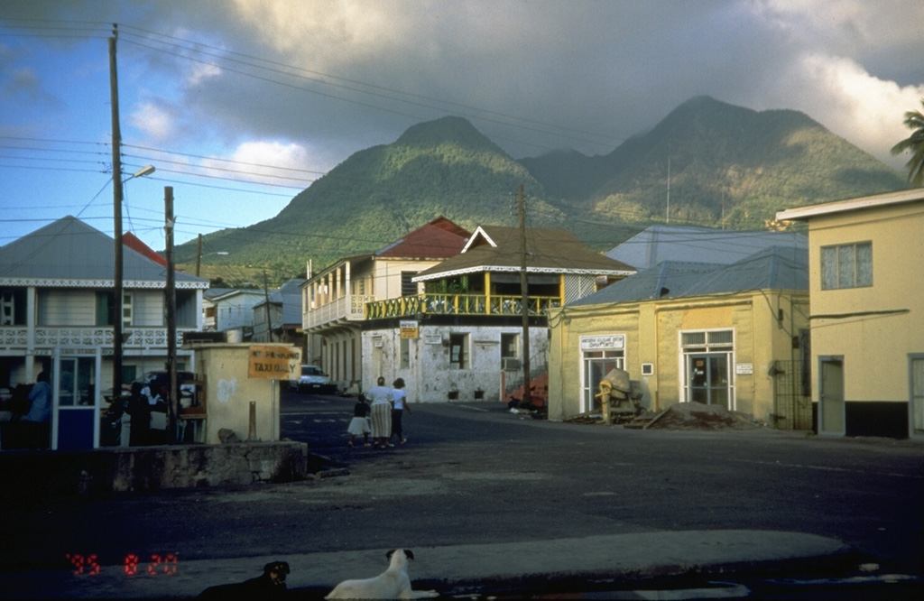 The summit of Soufrière Hills volcano towers above the streets of Plymouth, the capital city of Montserrat Island.  Plymouth is located only 4 km west of the volcano, on relatively flat pyroclastic-flow deposits from previous eruptions.  This photo was taken in August 1995, shortly after the start of a long-term eruption that severely impacted the island.  A lava dome that grew above the height of the crater rim produced pyroclastic flows that by August 1997 swept into the sea through the center of the evacuated city of Plymouth.  Photo by Cynthia Gardner, 1995 (U.S. Geological Survey).