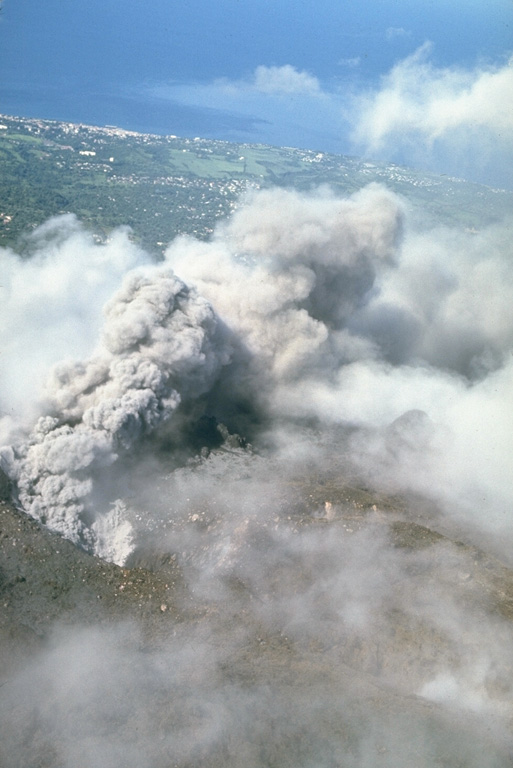 An ash column rises above a fissure on the upper NW flank of La Soufrière de la Guadeloupe volcano in October 1976, with the capital city of Basse-Terre in the background.  Intermmitent mild-to-moderate phreatic explosions took place from July 8, 1976, to March 1, 1977.  Concern about the possibility of a larger eruption prompted the evacuation of the capital city of Basse-Terre from August to November 1976.  Photo by Richard Fiske, 1976 (Smithsonian Institution).