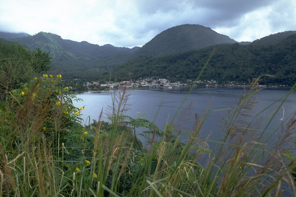 The town of Soufriere lies just NW of the 10-km-wide Qualibou caldera.  This view from the NW looks across Soufriere Bay to the rounded Terre Blanche lava dome.  The western caldera wall lies between the dome and the gentle ridge behind the town.  The ridge in the background to the left of Terre Blanche is the back wall of the 3.5 x 5 km caldera, which was formed during powerful eruptions about 32-39,000 years ago. Photo by Lee Siebert, 1991 (Smithsonian Institution).