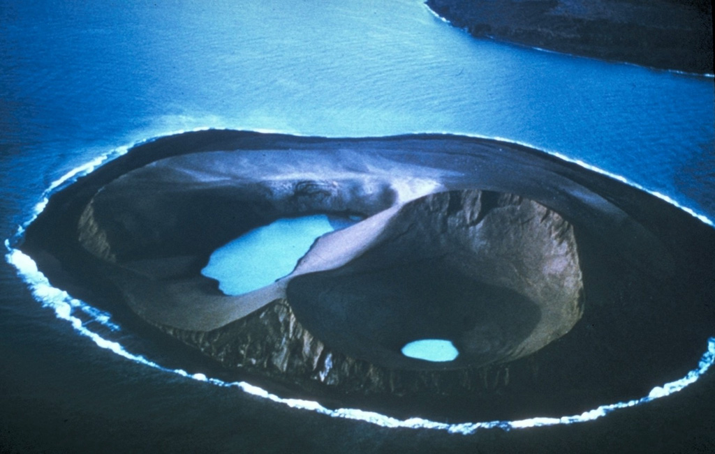 Water was present in two craters on Jolnir Island on 22 August 1966, less than two weeks after it ceased erupting. Jolnir was formed during repeated submarine eruptions that began in October 1965, immediately SW of the new island of Surtsey (upper right), rising above sea level and then being destroyed by erosion multiple times before it ceased activity on 10 August. No lava flows were produced, and a month after this photo was taken the loosely consolidated ash deposits that formed the island were eroded away. Photo by Richie Williams, 1966 (U.S. Geological Survey).