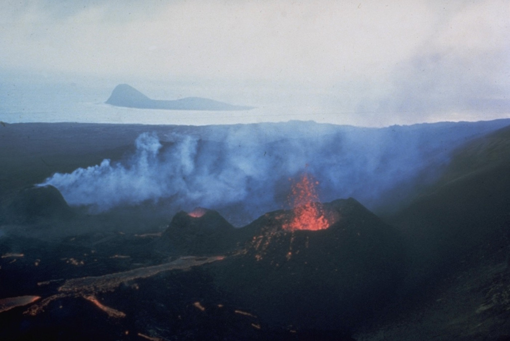 Lava flows issue from three small spatter cones on the island of Surtsey on 27 August 1966. Eruptions began in November 1963 and soon formed a new island, with lava effusion starting in April 1964. Eruptions at Iceland's newest island continued until 1967. The small island of Jolnir in the background began growing 800 m SW at the end of October 1965. It went through repeated episodes of growth and destruction before it ceased activity on 10 August 1966 and was eroded away by October. Photo by Richie Williams, 1966 (U.S. Geological Survey).