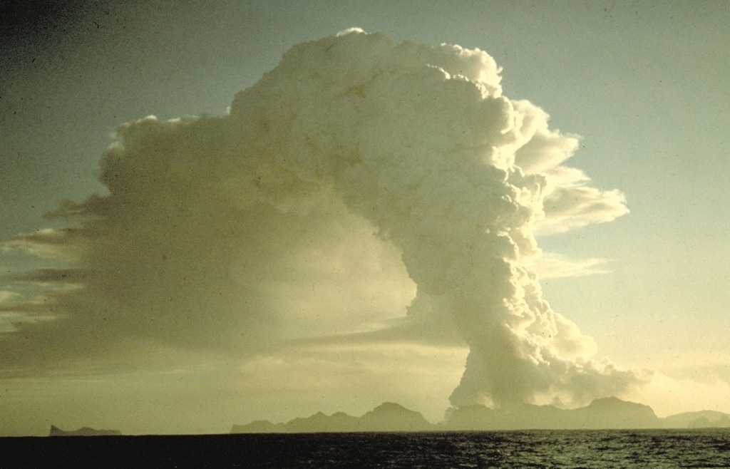 A column of steam and ash towers above the island of Heimaey on January 25, 1973, two days after the onset of its famous eruption.  The mostly submarine Vestmannaeyjar is the southernmost volcanic system in the eastern volcanic zone of Iceland.  It consists of a roughly 30 x 40 km group of volcanic islands and submarine cones occupying a shallow shelf off Iceland's southern coast.  Vestmannaeyjar was the site of two of Iceland's most noted 20th-century eruptions, at Surtsey during 1963-67 and at Heimaey in 1973. Copyrighted photo by Katia and Maurice Krafft, 1973.