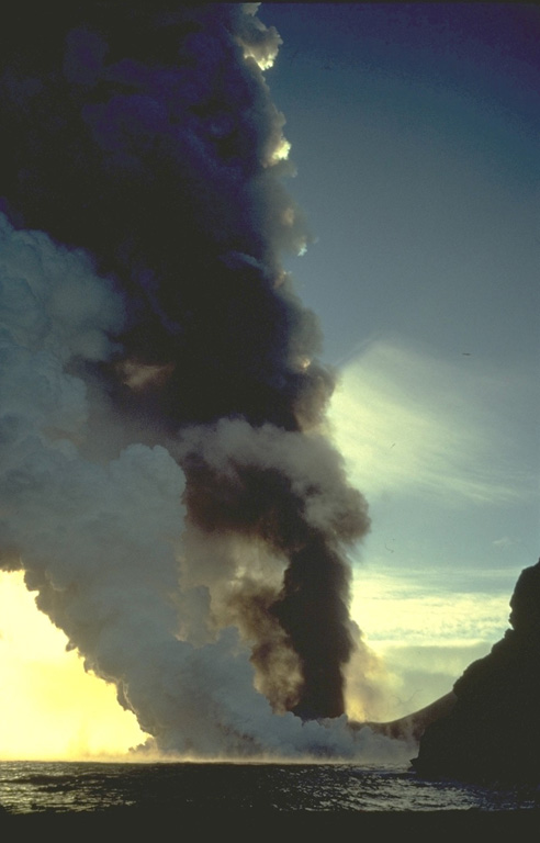 A thick column of steam rises above a lava flow that is entering the sea along the coast of Heimaey Island in January 1973.  The lava flow reached the sea during the first day of the eruption.  Concern that the flow would seal off the island's only harbor prompted the evacuation of all but essential personnel from the island.  Nearly all of the island's 5000 residents were evacuated the first night of the eruption. Copyrighted photo by Katia and Maurice Krafft, 1973.