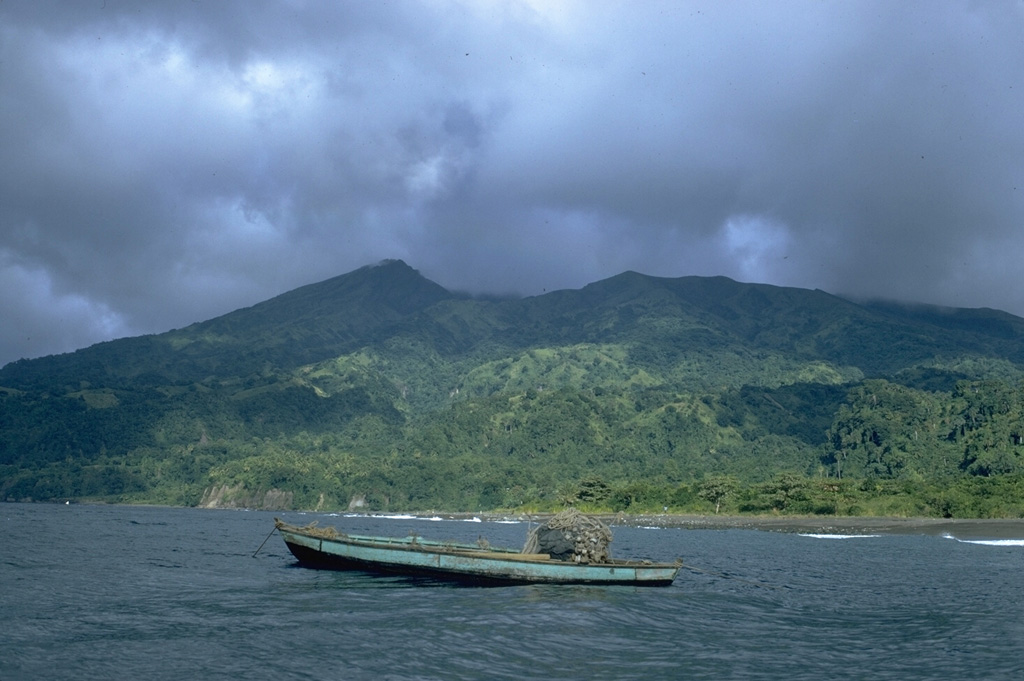 Soufrière St. Vincent volcano forms the northern end of the island of St. Vincent.  The 1178-m-high stratovolcano, seen here from off the west coast, has a broad summit.  The peak at the left, the volcano's high point, is the NW rim of a large crater created by a massive volcanic landslide.  The present-day, 1.6-km-wide summit crater truncates a cone (forming the flat-topped area across the saddle to the right) that was constructed within the earlier crater.  Several powerful explosive eruptions have occurred in historical time since 1718.  Photo by William Melson, 1972 (Smithsonian Institution).