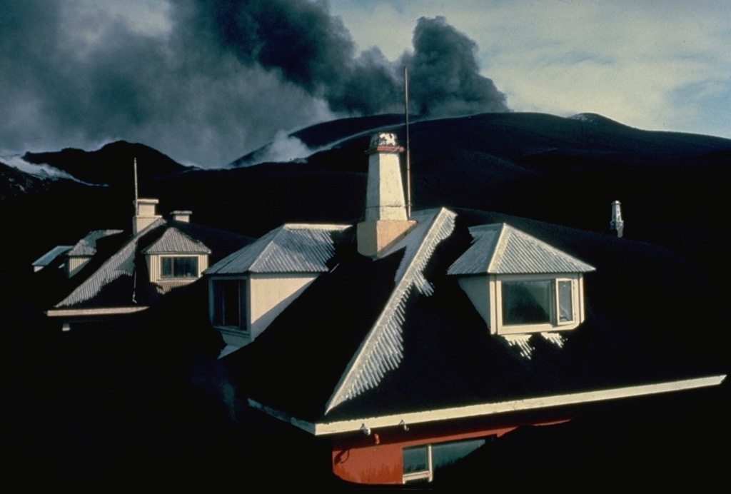 Eldfell cinder cone spews ash in the distance above the town of Vestmannaeyjar in April 1973.  Thick ashfall deposits from the the volcano buried houses in the town.  Most of the 5000 residents of the island were evacuated during the initial night of the eruption, which began on January 23.  By the time the eruption ended on June 28, the volcano had ejected 0.02 cu km of ash, most of which fell out to sea.  Following the eruption, 550 prefabricated houses were brought in from Scandinavian countries and Canada. Copyrighted photo by Katia and Maurice Krafft, 1973.