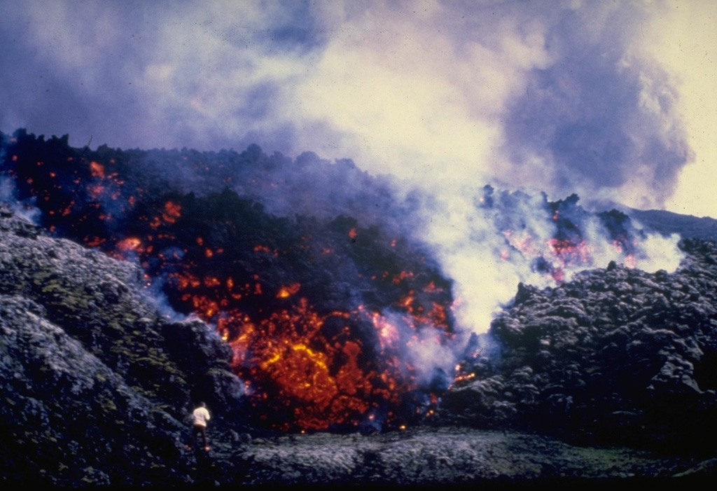 A volcanologist can be seen (bottom left) observing the incandescent front of a steaming, blocky lava flow that is advancing from Hekla volcano during a three-day eruption beginning on 17 August 1980. Lava issued from much of the 5.5-km-long fissure that runs along Hekla’s summit ridge, producing lava flows that covered much of the northern flanks and flows to the E, S, and SW. Photo courtesy of Gudmundar Sigvaldason (Nordic Volcanological Institute), 1980.