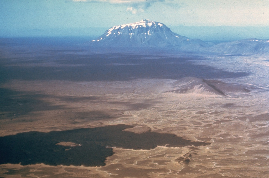 The dark Vikrahraun lava flow in the foreground was erupted from the NE side of Askja caldera in 1961. The flat-topped mountain in the distance to the NE is Herdubreid, the most famous of Iceland's "table mountains." These steep-sided mountains were formed by repeated eruptions during the Pleistocene through the glacial icecap. The subglacial lava flows and fragmental hyaloclastite rocks ponded against the melted walls of the glacier. Only at the last stage were minor subaerial lavas erupted above the icecap, forming the small summit peak. Photo by Richie Williams, 1973 (U.S. Geological Survey).