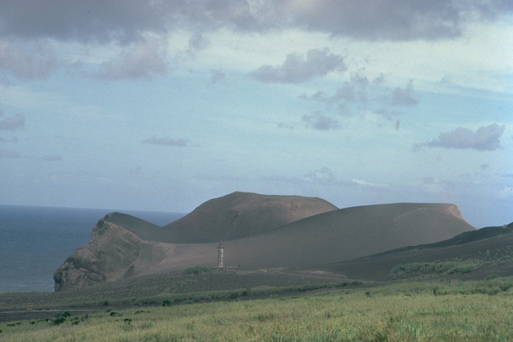 A pyroclastic cone initially built by submarine eruptions during 1957-58 now forms a peninsula at the western tip of Fayal Island.  The top of the lighthouse, which was located along the former shoreline, is visible at the lower left-center of the photo.  Heavy ashfall from the eruption covered several houses and partially buried the lighthouse.  Within the first two weeks of the eruption, an 800-m-wide island was built up to 100 m above sea level.   Copyrighted photo by Katia and Maurice Krafft, 1980.