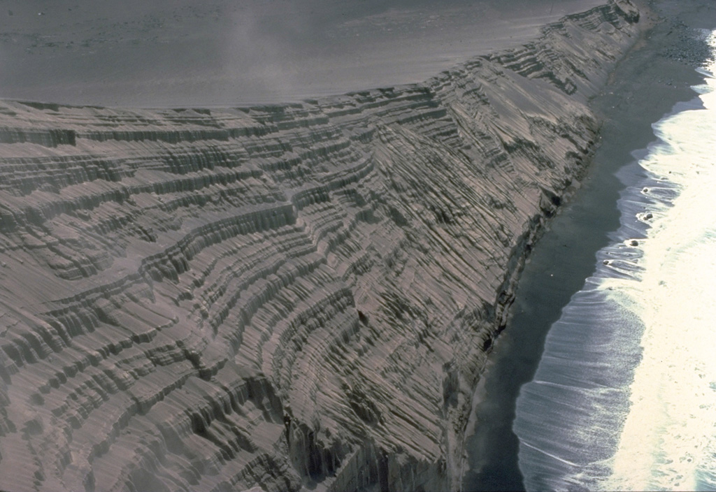 The new pyroclastic cone formed during the 1957-58 Capelinhos eruption has been extensively eroded by the sea, exposing this cross-section of the cone.  The thick stack of tephra layers formed by fallout of pyroclastic material during individual eruptive pulses illustrates the process by which pyroclastic cones grow.  Initial eruptions were submarine, but these tephra layers were formed by subaerial eruptions after the vent rose above sea level. Copyrighted photo by Katia and Maurice Krafft, 1980.