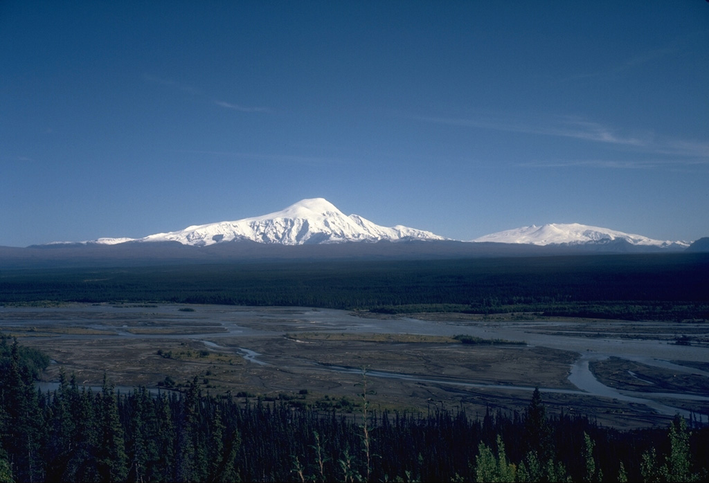 This view, across the Copper River to the SE, shows Mount Sanford (left) and Mount Wrangell (right). The eroded Sanford shield volcano has a broad, rounded top that is surrounded by steep glacial cirques. Most of the volcano formed during the Pleistocene. Eruptive activity at Wrangell has continued into historical time. Photo by Donald Richter (Alaska Volcano Observatory, U.S. Geological Survey).