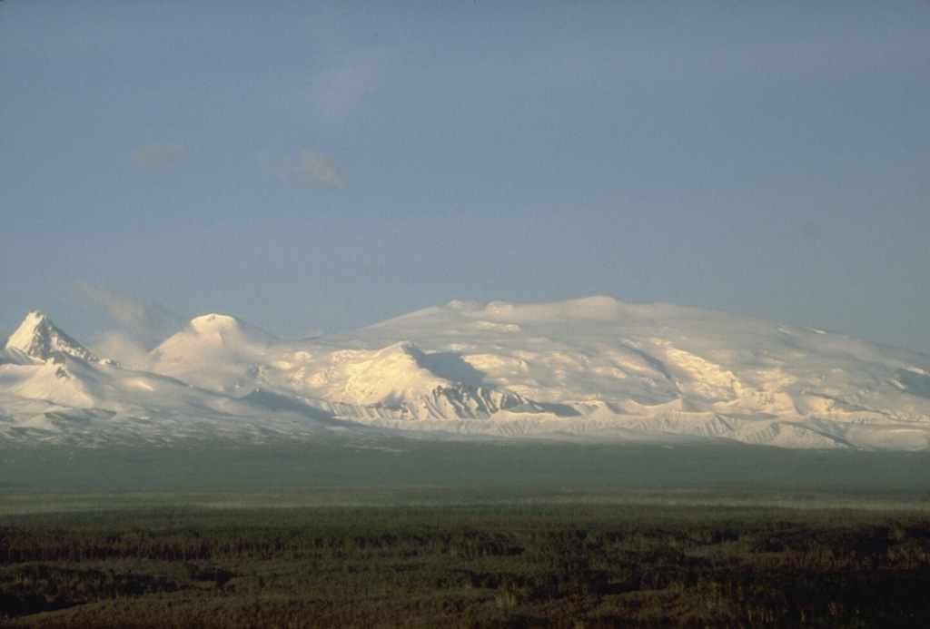 Mount Wrangell, on the right skyline, is part of the Wrangell volcanic field. There are two large calderas at the summit and the inner ice-filled caldera contains three craters. Minor, possibly phreatic eruptions have occurred during the 20th century. To the left is rounded Mount Zanetti, a flank cone. The sharp-topped peak to the far-left of this view from the SW is a flank cone of the neighboring Pleistocene Mount Drum. Photo by B. Cella (National Park Service).