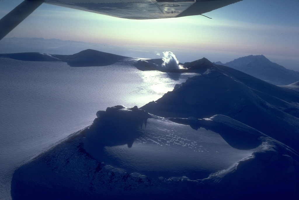 An aerial view shows a portion of the 4 x 6 km, ice-filled, summit caldera of Mount Wrangell. It is the part of the Wrangell volcanic field and has documented historical eruptions. Fumaroles (right-center) remain active at one of three scoria cones on the caldera rim. Photo by Chris Nye (Alaska Division of Geological and Geophysical Surveys, Alaska Volcano Observatory).