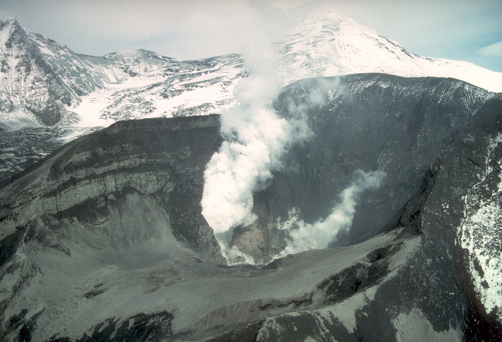 Crater Peak crater on Mount Spurr is seen here producing a plume on 18 June 1992, the day after a brief violent explosion. Fresh deposits are on the interior of the crater and the pre-eruption crater lake is gone. The summit is visible behind the plume to the upper right in this view from the south. Photo by Chris Nye, 1992 (Alaska Division of Geological and Geophysical Surveys).