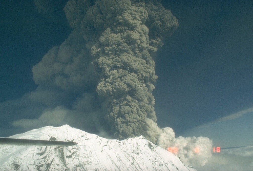 The second of three large explosive eruptions from Crater Peak, a satellite cone of Mount Spurr, 3.2 km south of the peak, occurred on 18 August 1992. This aerial view from the west shows the base of the vertical eruption plume that reached an altitude of about 13.5 km. This eruption lasted about 4.5 hours and resulted in ashfall in Anchorage, 125 km E, that resulted in closure of the international airport for 20 hours.  Photo by Game McGimsey, 1992 (Alaska Volcano Observatory, U.S. Geological Survey).