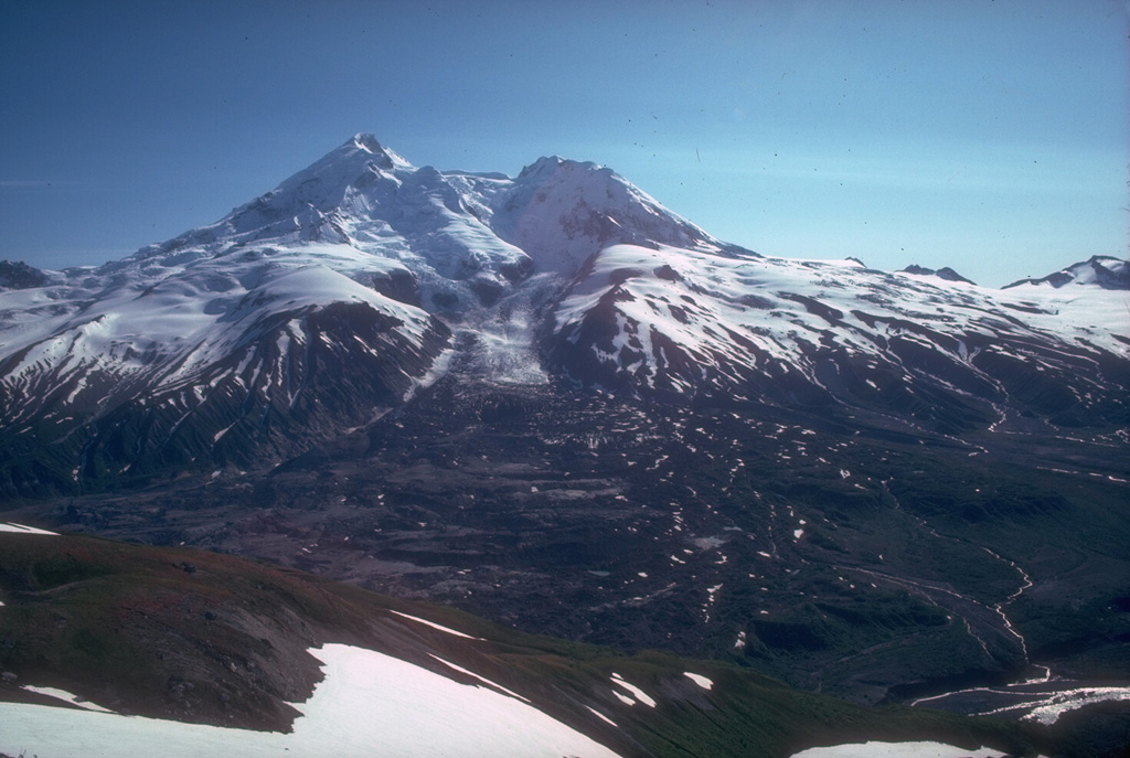 Redoubt is one of the most active volcanoes of the upper Cook Inlet region, viewed here from the north in 1980. Drift glacier flows from the summit into the Drift River valley. Thick lava flows partly form the summit and Holocene lahars have filled the Drift River valley to the NE and Crescent River valley to the SE. Photo by Allison Till, 1980 (Alaska Volcano Observatory, U.S. Geological Survey).