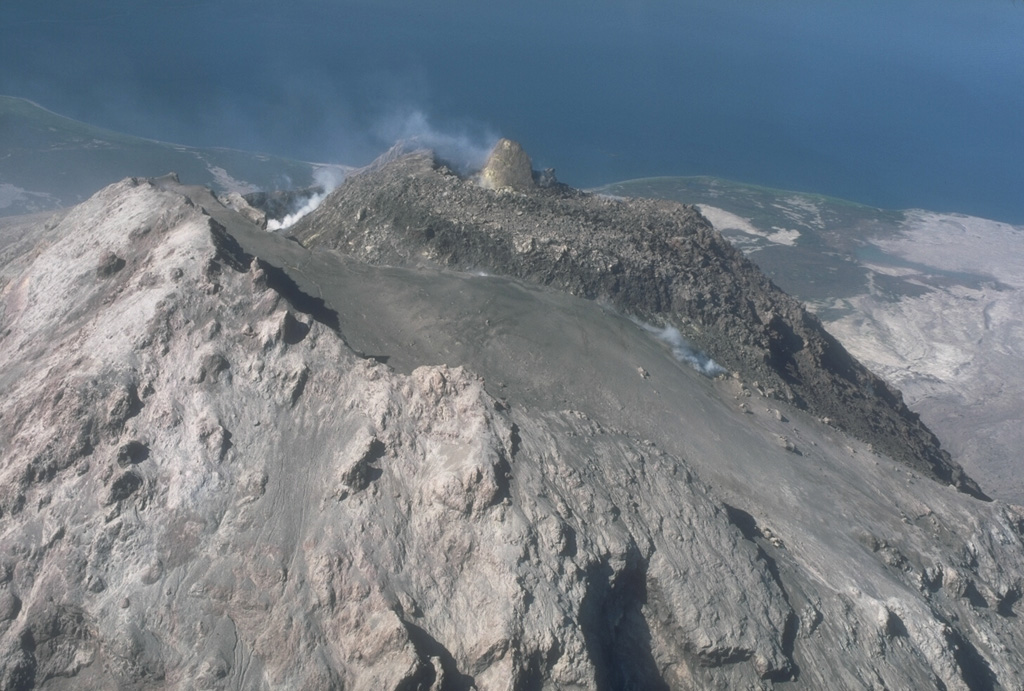 A 50-m-high spine formed on the 1986 lava dome at Augustine, seen here in 1987. The lava dome at the summit formed within an arcuate crater on the 1976 dome. As seen in this view from the SE, the surface of the 1976 dome is covered with pyroclastic ejecta from the 1986 eruption. The high point of the volcano (left) is a crater rim of the 1964 dome. Photo by Alaska Volcano Observatory, U.S. Geological Survey, 1987.