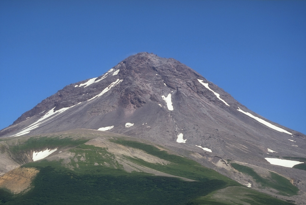 The summit lava dome complex of Augustine volcano is seen here above its SW flank. The upper part of the summit is a lava dome from the 1963-64 eruption. Pre-Augustine sedimentary basement rocks of Jurassic to Tertiary age are exposed on the south flank to an elevation of 320 m. Photo by Game McGimsey, 1994 (Alaska Volcano Observatory, U.S. Geological Survey).