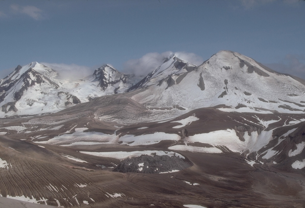 Trident, seen here from Baked Mountain to its NW, was initially named for its three prominent summits. A series of eruptions from 1953 until 1968 constructed a fourth cone, which forms the smoother peak to the right. As many as 23 lava domes are found in the Trident volcanic complex. The 1912 Novarupta lava dome is visible to the lower center. Photo by Game McGimsey (U.S. Geological Survey, Alaska Volcano Observatory).