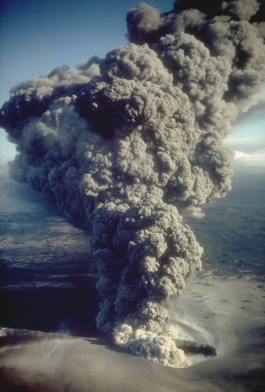 An ash plume erupts from eastern crater of the newly formed Ukinrek Maars on 6 April 1977. West Maar formed during the initial days of the eruption that began on 30 March. Three days later explosions began at East Maar, 600 m away. At the peak of the eruption ash plumes reached up to 6 km above the vent. On the 4th day of the eruption a lava dome appeared within East Maar. Photo by R. Russell, 1977 (Alaska Department of Fish and Game).