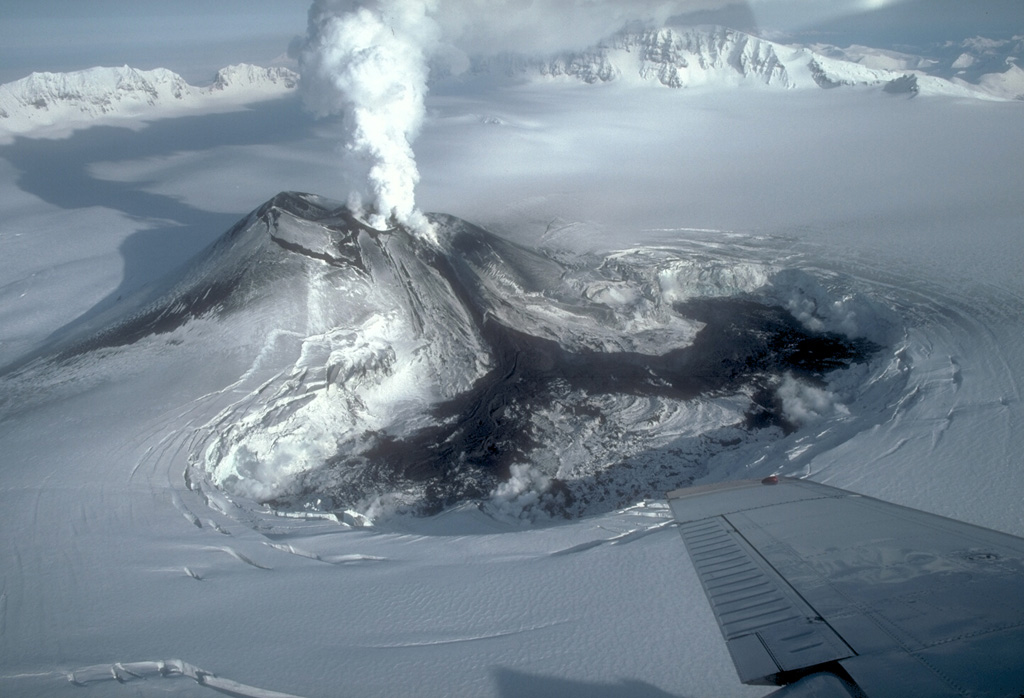 On 23 January 1984 this black lava flow erupted from a scoria cone in the west side of Veniaminof caldera, traveled down the south flank, and diverged into two lobes as it melted through glacial ice on the caldera floor. Strombolian eruptions began on 2 June 1983 and continued until the end of the eruption on 17 April 1984. By the time of this photo the lava flow had melted a depression about 1 x 2 km wide and 120 m deep. The NE caldera wall rises 500 m above the icecap in the distance. Photo by Betsy Yount, 1984 (Alaska Volcano Observatory, U.S. Geological Survey).