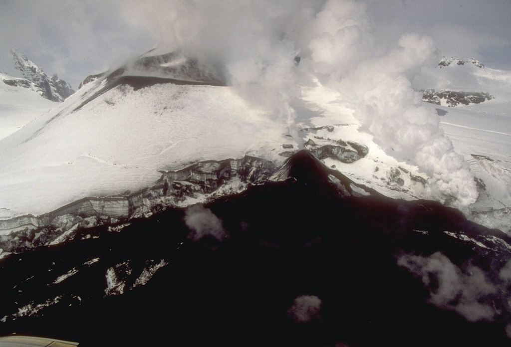 A new lava flow accumulates at the base of a scoria cone in Veniaminof caldera. This 9 May 1994 view from the west shows the snow-covered cone and the lava flow, which has melted through the glacial icecap on the caldera floor. Photo by Chris Nye, 1994 (Alaska Division of Geological and Geophysical Surveys).