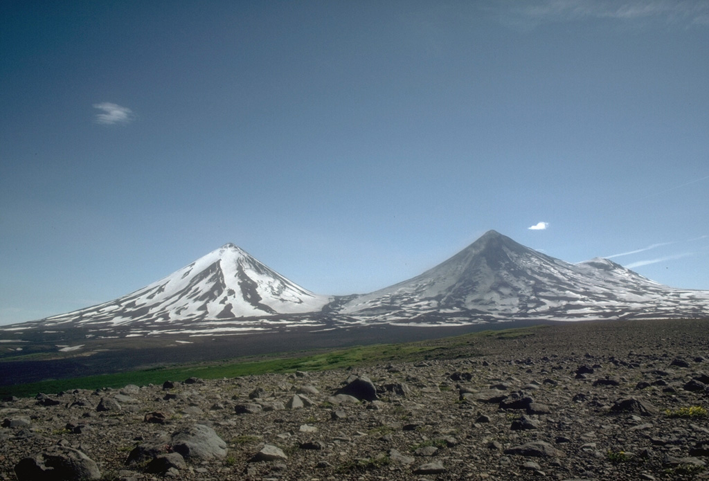 The summits of Pavlof Sister (left) and Pavlof (right) rise above a roughly 1,100-m-elevation saddle. They are viewed here in 1975 from lowlands to the NW. Pavlof is darkened by recent ash deposition and has been the source of frequent eruptions in historical time. Little Pavlof, a cone on the right flank of Pavlof, was also constructed along a line of vents trending NE from Emmons Lake caldera. Photo by Tom Miller, 1975 (Alaska Volcano Observatory, U.S. Geological Survey).