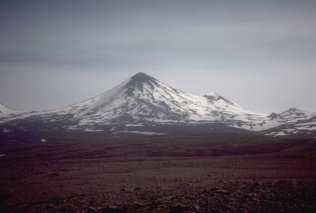 Pavlof, rising above low plains to its NW, is one of Alaska's most active volcanoes. It is part of a NNE-SSW-trending line of volcanoes near the tip of the Alaskan Peninsula. Little Pavlof is the small cone on the right horizon. The low saddle to the left separates Pavlof from Pavlof Sister, whose lower flanks are seen to the far left. Photo by Steve McNutt, 1979 (University of Alaska, Alaska Volcano Observatory).