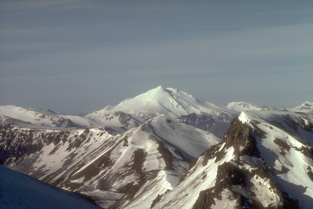 Mount Dutton, seen here from the NE with the wall of Emmons Lake caldera in the foreground, is located near the tip of the Alaska Peninsula. Successive lava domes form the summit; collapse events during the Holocene produced debris avalanches that traveled to the west and also reached Belkofski Bay to the south. Photo by Betsy Yount, 1986 (Alaska Volcano Observatory, U.S. Geological Survey).