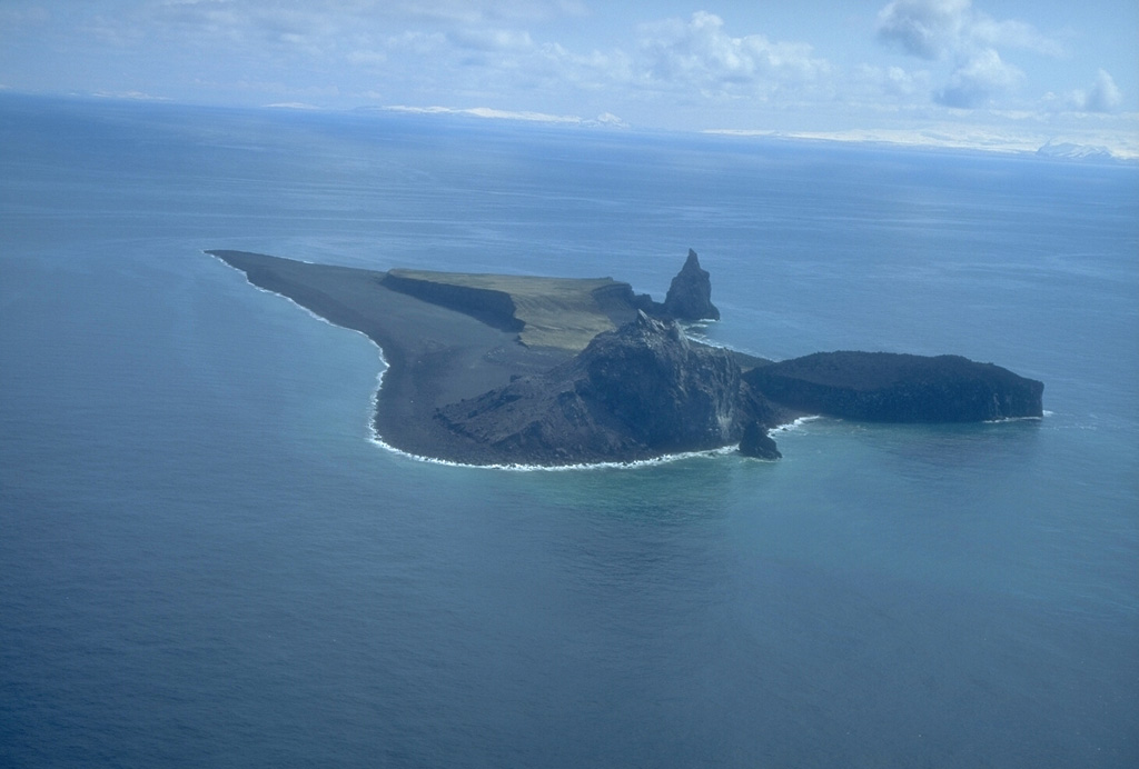 Bogoslof is the summit of a largely submarine volcano located in the Bering Sea, 50 km behind the main Aleutian arc. The island is about 1.5 x 0.6 km wide and due to its frequent eruptive activity and energetic wave action, has changed shape dramatically since it was first mapped in the late 1700s. The rounded lava dome and offshore spire at the northern tip of the island (bottom-center) formed in 1992. The circular, flat area at the right is a remnant of the 1927 lava dome, and the steep pinnacle is Castle Rock, a 1796 dome remnant. Photo by Terry Keith, 1994 (Alaska Volcano Observatory, U.S. Geological Survey).