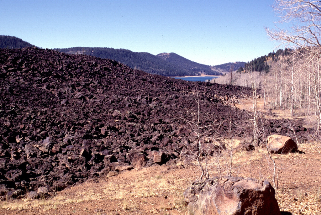 A group of basaltic cinder cones and lava vents on the Markagunt Plateau east of Cedar Breaks National Monument has produced youthful, sparsely vegetated lava flows.  Several lines of NE-SW-trending cinder cones are present within the volcanic field, with the youngest flows occurring near Panguitch Lake on the north and Navajo Lake on the south.  Navajo Lake (upper right) formed when a thick, blocky flow from a nearby vent dammed Duck Creek.  The oldest trees on the youngest flows are about 900 years old. Photo by Lee Siebert, 1996 (Smithsonian Institution)