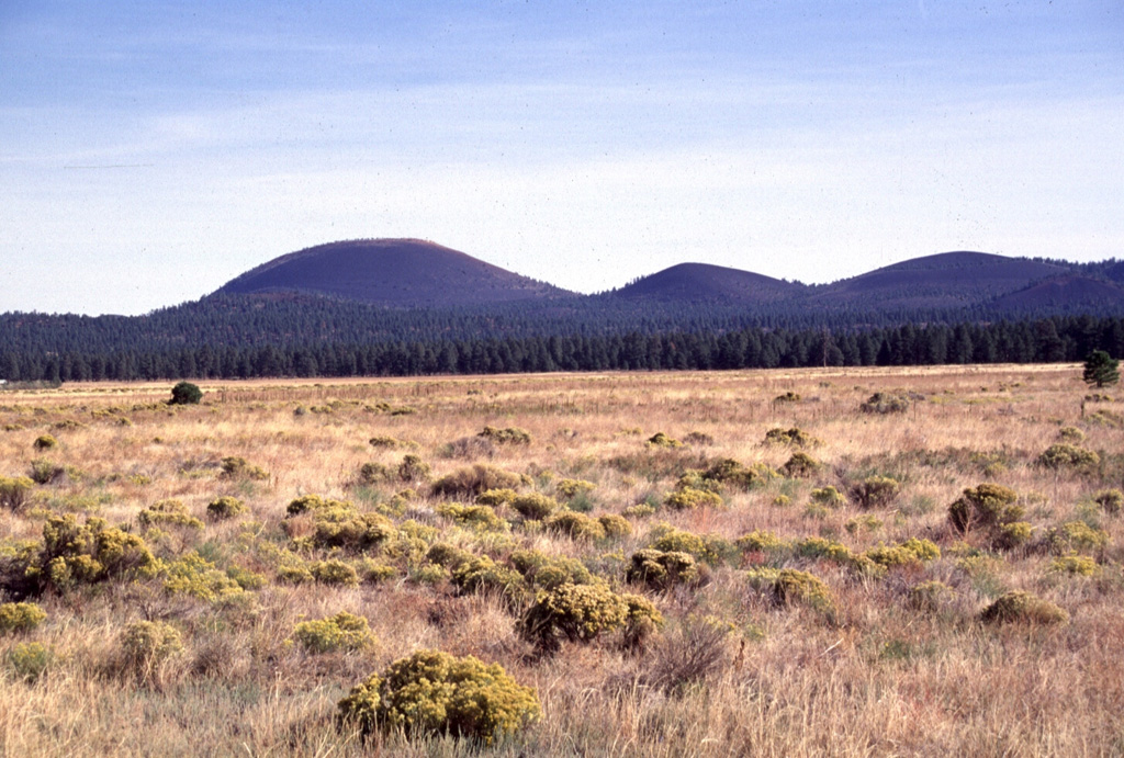 Sunset Crater (left) and adjacent cinder cones are seen here from the west across the meadows of Bonito Park.  Sunset Crater and adjacent cones were erupted along a 10-km-long, NW-SE-trending line, with Sunset Crater being the NW-most vent.  The Sunset Crater eruptions severly affected Sinagua Indians living in the area, who temporarily evacuated the region. Photo by Lee Siebert, 1996 (Smithsonian Institution).