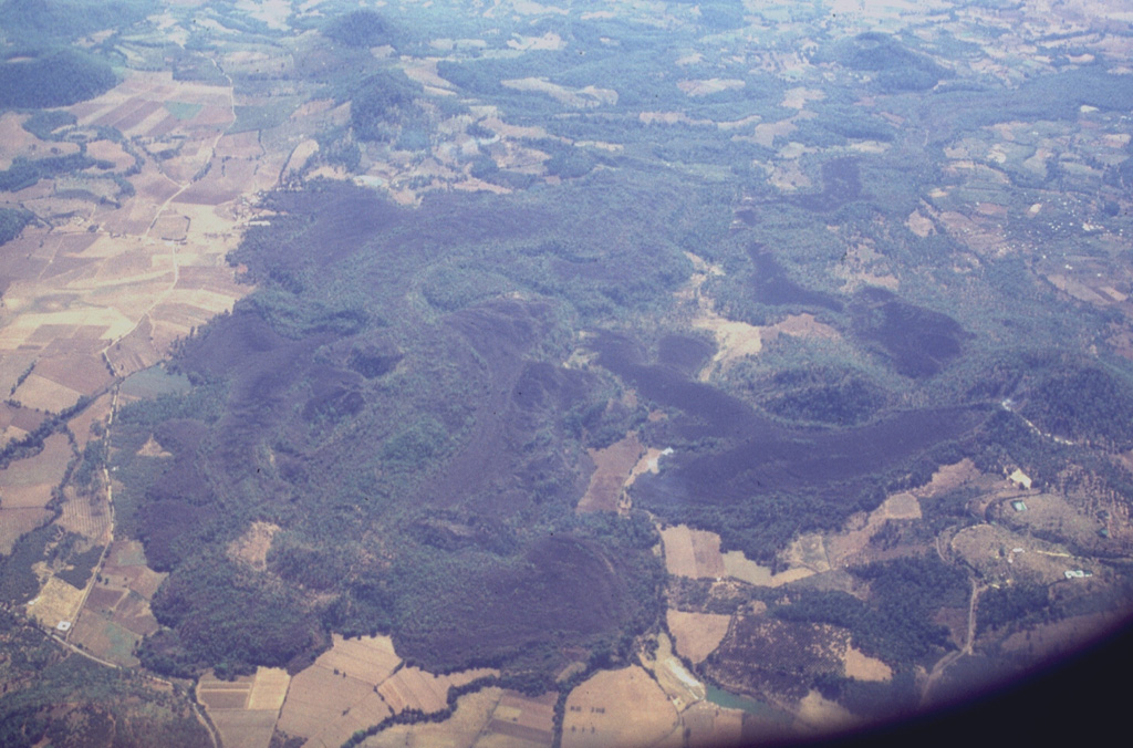 Lava flows in the western part of the Michoacán-Guanajuato volcanic field are seen here from the north. Cerro el Astillero, a scoria cone near the middle right-hand margin of the photo, was the source of the unvegetated lava flow that extends to the east and then south. Cerro el Pedegral, a cone near the lower left, produced lava flows to the west and south toward the upper part of the photo. This lava field is located near the town of Tancítaro and is among the many Holocene flows in the Michoacán-Guanajuato field. Photo by Lee Siebert, 1997 (Smithsonian Institution).