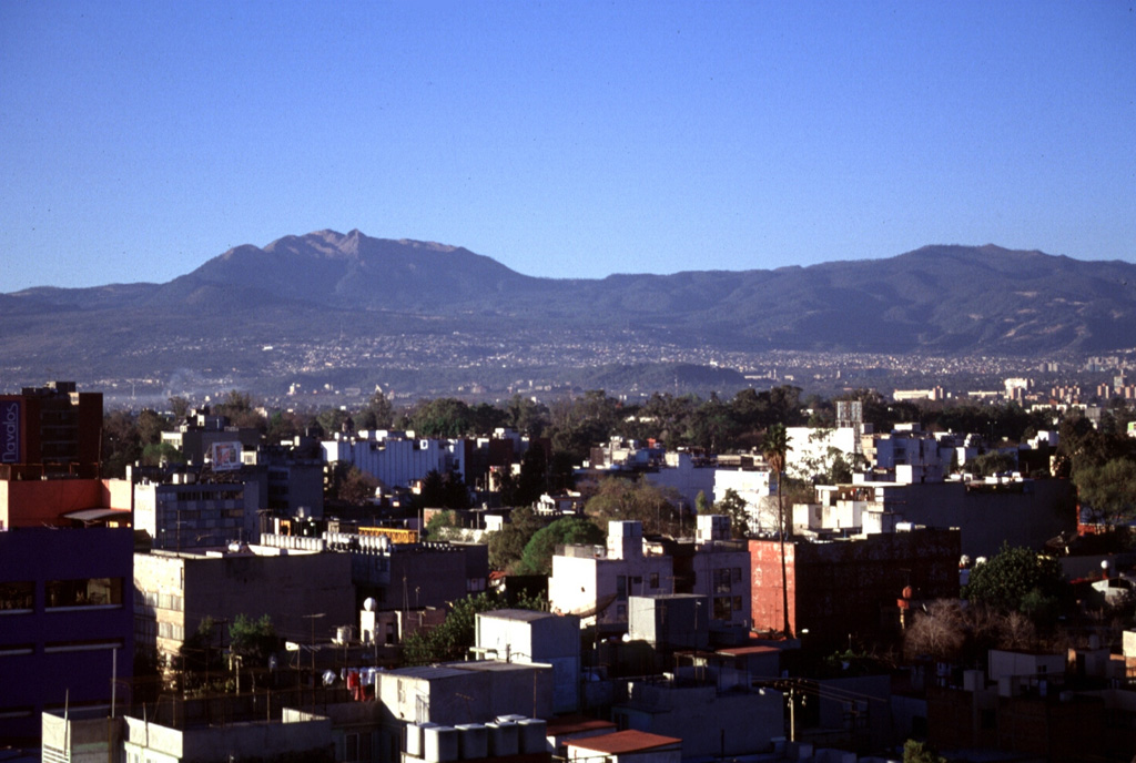 Ajusco volcano rises above Mexico City to the south. The Chichinautzin volcanic field covers a broad, 1,000 km2 area with more than 150 small cones of mostly Holocene age. One of the youngest eruptions occurred from the Xitle cone about 1,670 years ago, producing a massive 3.2 km3 lava flow that covered prehistorical urban centers and agricultural land. It is now overlain by the southern part of Mexico City. Photo by Lee Siebert, 1997 (Smithsonian Institution).