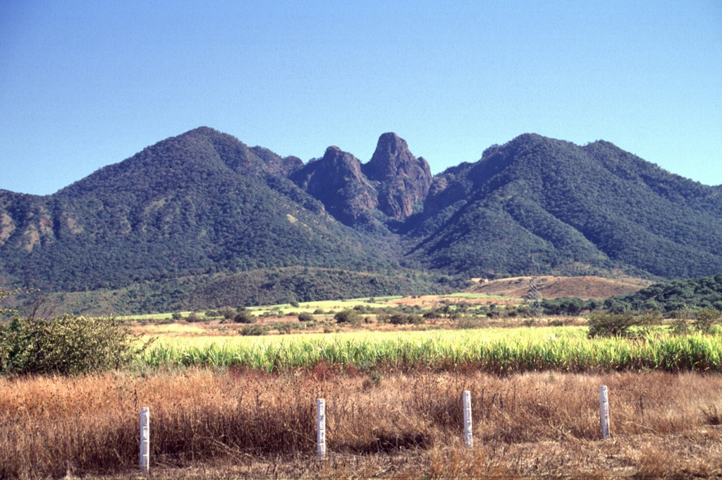 The steep remnant at Sangangüey volcano (center) rises 250 m above the Arroyo Caracol, an erosional valley down the SW flank. It is similar in composition to surrounding layered lava flows, but contains less glass, which suggests slower cooling. The Arroyo Caracol exposes a 700-m-thick section showing the interior stratigraphy of the cone. Photo by Lee Siebert, 1997 (Smithsonian Institution).